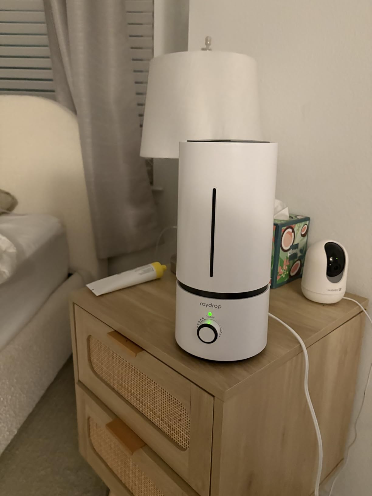 White Raydrop humidifier on a bedroom nightstand next to a lamp, a tissue box and a baby monitor