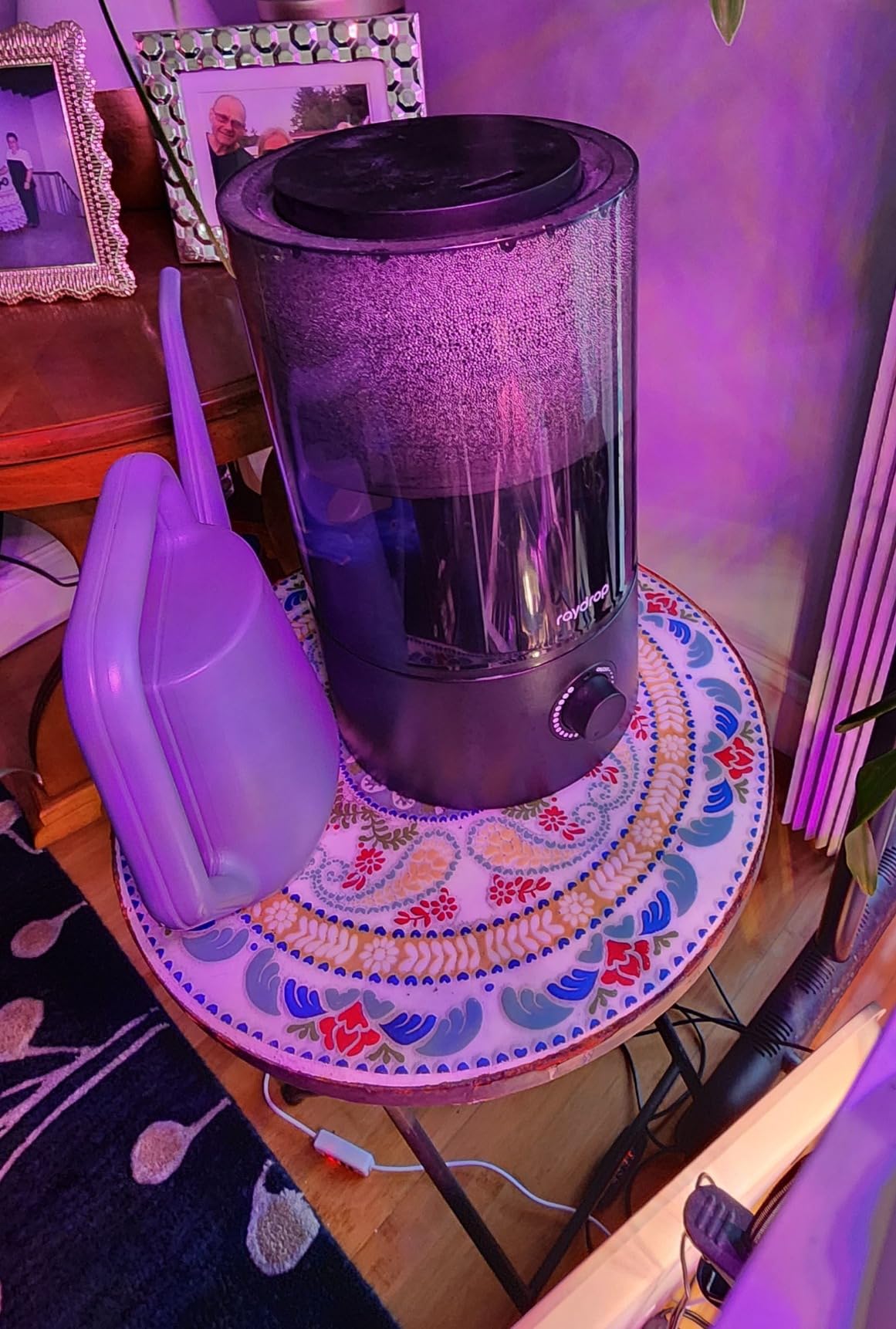 Black Raydrop humidifier on a mosaic side table beside a watering can, lit by a purple grow light