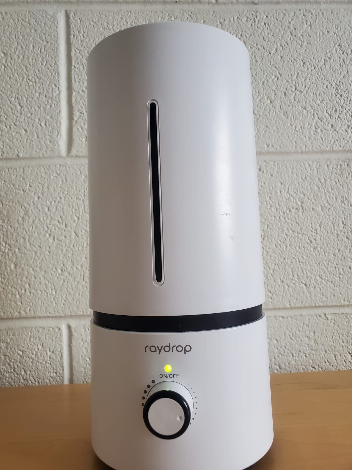 White Raydrop humidifier with a rotary dial and green power light on a desk against a painted brick wall